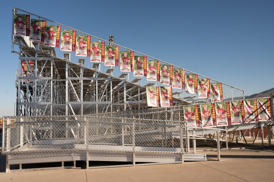 End and rear view of an elevated aluminum grandstand showing the full understructure framing and chain link guardrail hung with senior player banners.